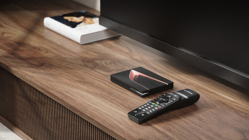Formuler Z12 Ultra streaming media player and BT3 remote on wooden media console next to a book and TV.